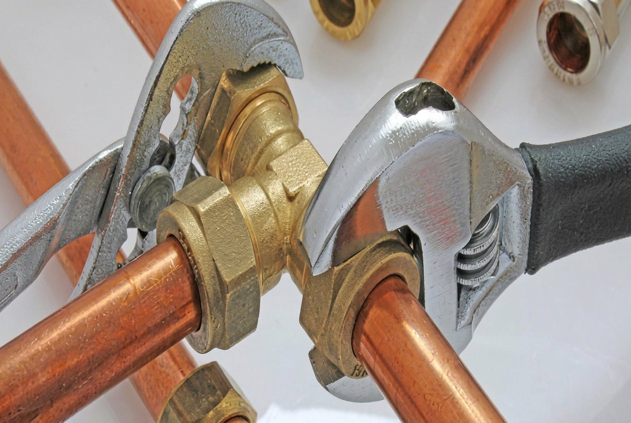 Copper plumbing pipework and brass fittings being tightened with two wrenches