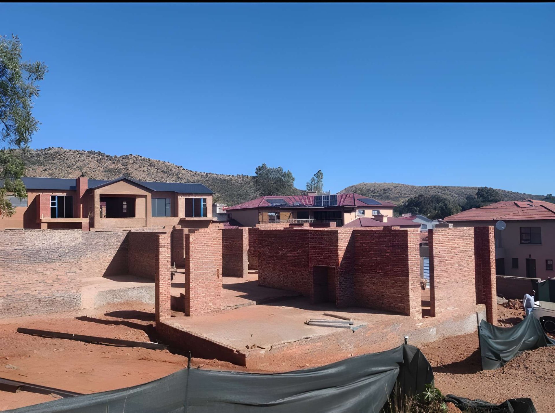 Wide view of a face-brick residential structure under construction with hills behind it
