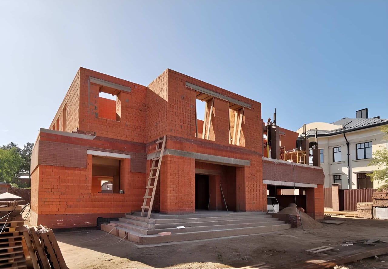 Red-brick double-storey residence under construction with window openings framed and a ladder on site